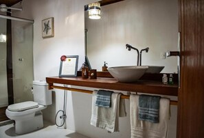 A bathroom with a white toilet, a wooden vanity with a sink, a mirror, and towels hanging on a rack. - Pousada Barra Suítes (Maraú)