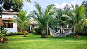 Un jardín con una hamaca, palmeras y un edificio con techo de tejas.