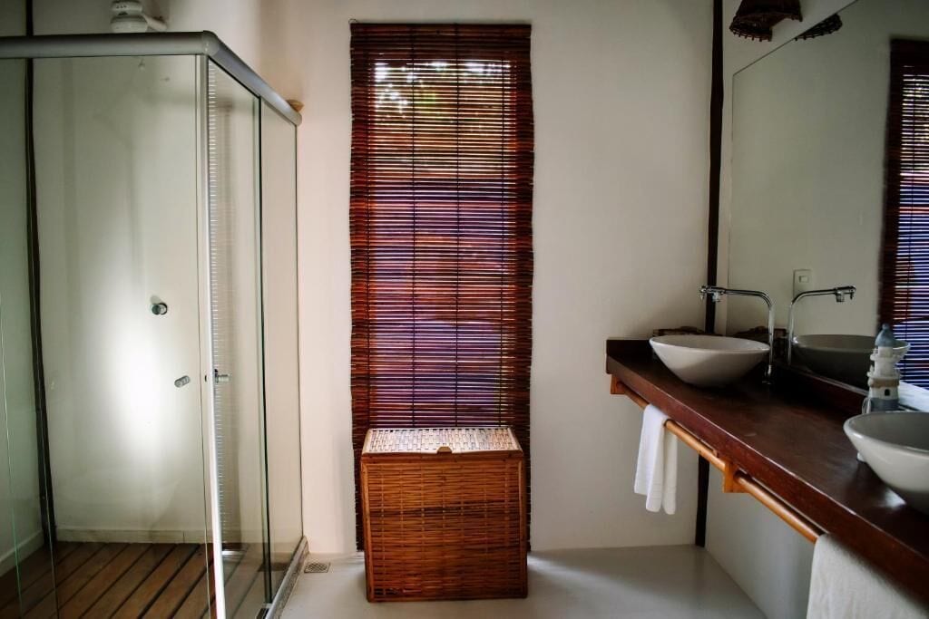 Een badkamer met een douchecabine van glas, een houten mand en een wastafel met een spiegel erboven.