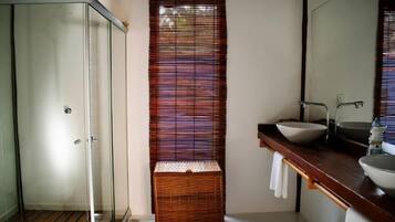 Een badkamer met een douchecabine van glas, een houten mand en een wastafel met een spiegel erboven.
