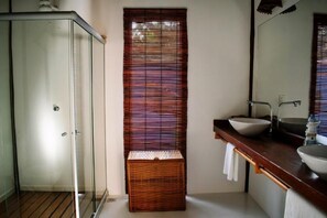 Une salle de bain avec une douche à parois de verre, un panier en bois et un lavabo avec un miroir au-dessus.