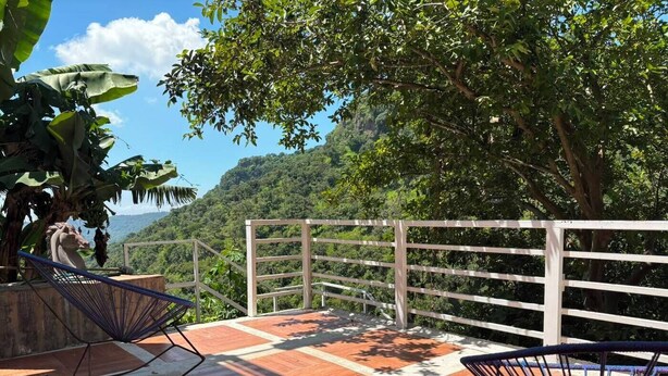 Una terraza con vistas a un paisaje montañoso, barandilla blanca y dos sillas.