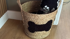 Een gevlochten mand met een zwart-wit pootafdrukpatroon, op een houten vloer voor een muur.