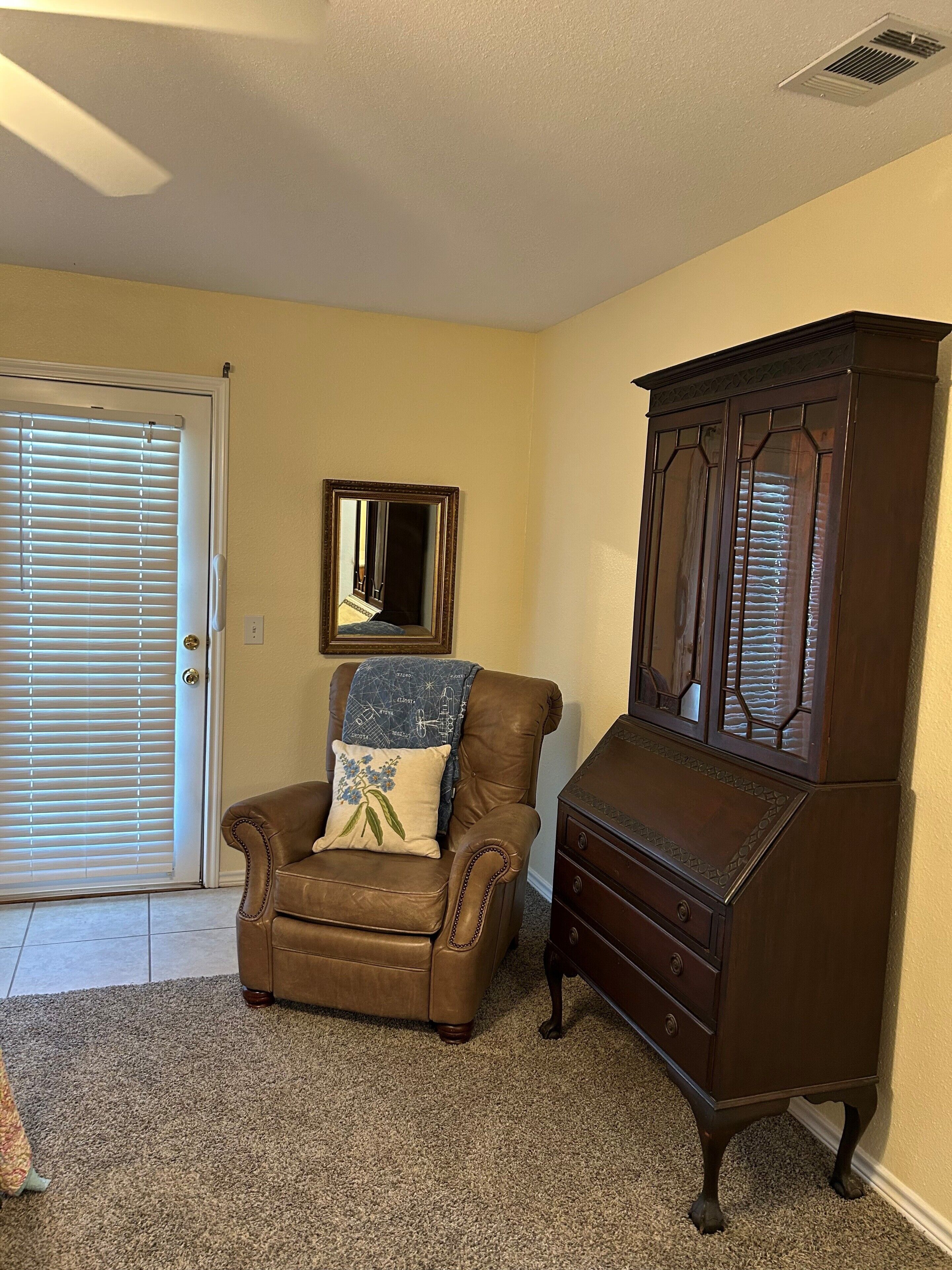 A room with a brown leather chair, a wooden cabinet, and a door with blinds.