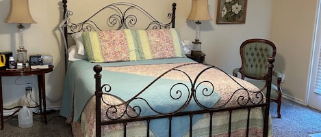 Un dormitorio con una cama, dos mesitas de noche, una silla, un ventilador de techo y una lámpara de pared.