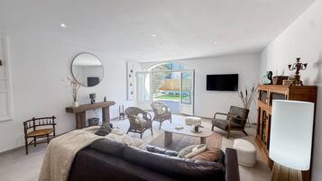 Een moderne woonkamer met een bank, fauteuils, een salontafel, een televisie en een groot raam.