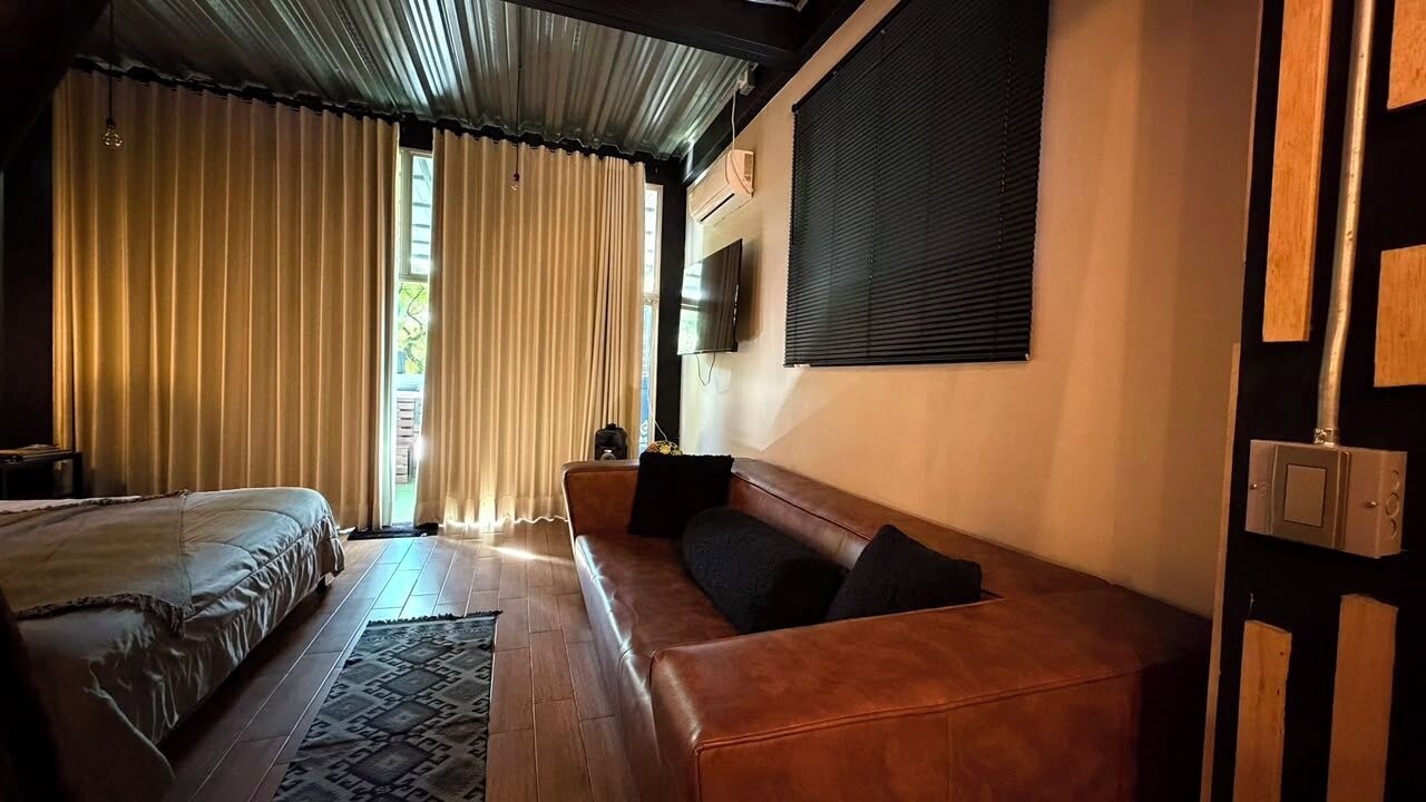 A room with a bed, a sofa, a television mounted on the wall, and a window with curtains.