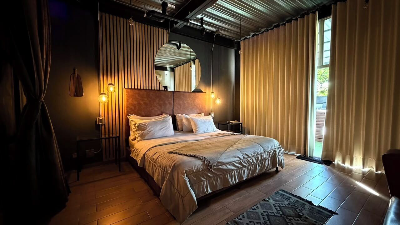 A bedroom with a large bed, a headboard, bedside tables, a mirror, and curtains.