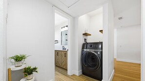 A laundry area with a washing machine, wooden flooring, and white walls. - Family Oasis • Playset • Near Airport & Stadium (Tampa)