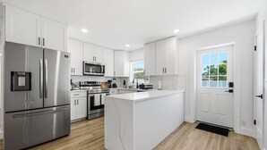 A modern kitchen with white cabinetry, stainless steel appliances, and a marble island. - Family Oasis • Playset • Near Airport & Stadium (Tampa)