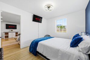 Ein Schlafzimmer mit einem Bett, einem an der Wand befestigten Fernseher, einem Fenster und einer Tür zu einem Badezimmer.