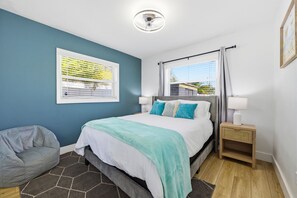 Ein Schlafzimmer mit Bett, Sitzsack, Nachttisch, einem Fenster mit Vorhängen und einer Deckenleuchte.
