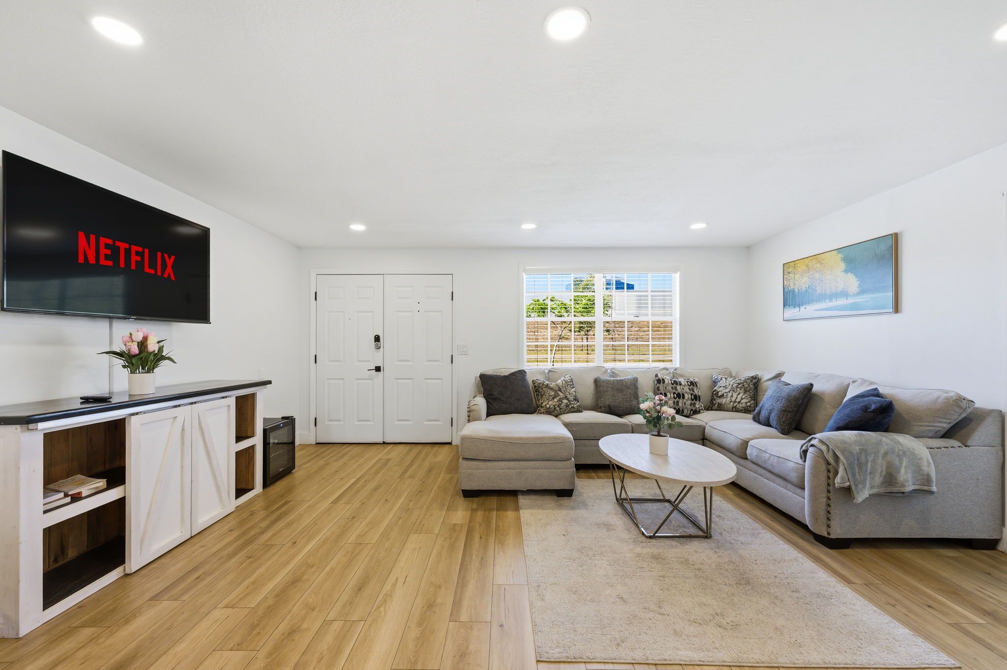 A living room with a flat-screen TV, a sofa, a coffee table, and a window with blinds.
