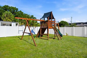 Ein hölzerner Spielplatz mit Kletterwand und Rutsche in einem Garten.