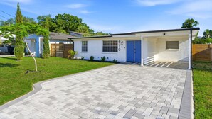 A single-story house with a blue door, a covered porch, and a paved driveway. - Family Oasis • Playset • Near Airport & Stadium (Tampa)