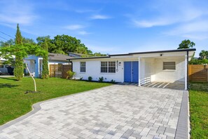 Ein eingeschossiges Haus mit blauer Tür, einer überdachten Veranda und einem gepflasterten Auffahrt.