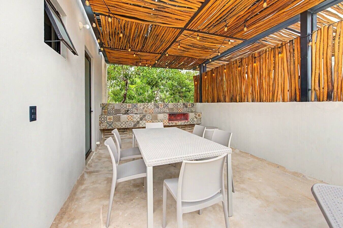 Une terrasse extérieure avec une table et des chaises, un mur décoré de motifs et une structure de plafond en bois.