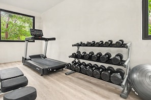 A gym with a treadmill, dumbbells, and weight plates. - Jungle Park 3BR Home | Private Pool & Gym (Tulum)
