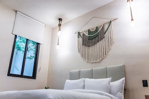 A bedroom with a bed, a window with a view of trees, a macrame wall hanging, and a ceiling light fixture. - Jungle Park 3BR Home | Private Pool & Gym (Tulum)