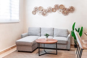 A modern living room with a grey sectional sofa, a round wooden coffee table, and a wall-mounted decorative arrangement. - Jungle Park 3BR Home | Private Pool & Gym (Tulum)