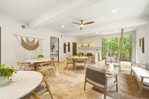 A spacious dining area with round tables and chairs, a ceiling fan, and a view of greenery outside. - Jungle Park 3BR Home | Private Pool & Gym (Tulum)