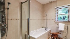 Ein Badezimmer mit Duschkabine, Badewanne und Fenster mit Jalousien.