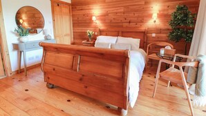 Ein Schlafzimmer mit Holzwandverkleidung, ausgestattet mit einem Bett, Nachttischen, einem Spiegel und einem Sessel.