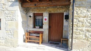 A stone building entrance with a wooden bench, a door, and a small stool.