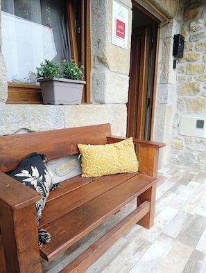 A wooden bench with a patterned cushion, a potted plant, and a stone wall with a sign.