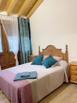 A bed with a wooden headboard, two pillows, a folded towel, and a bedside table with a lamp.
