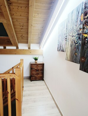A wooden staircase with a plant on a cabinet, a wooden ceiling, and a wall with a patterned painting.