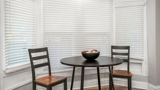 A dining area with a round table and two chairs, a bowl of snacks, and white window blinds. - Fresh and Cozy Mansion Near Downtown (Kansas City)