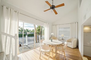 A spacious room with a ceiling fan, a dining table with chairs, a sofa, and a view of the outside through large windows. - Bayview Jr. 2 Bedroom Bungalow (Nokomis)
