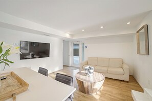 A modern living room with a flat-screen TV, a round coffee table, a sofa, and a dining area with chairs. - Bayview Jr. 2 Bedroom Bungalow (Nokomis)