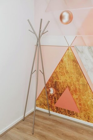 Een hoek met een vloerlamp, een geometrisch kunstwerk aan de wand en een houten vloer.