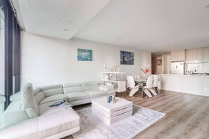 Een moderne woonkamer met een hoekbank, een eethoek met witte stoelen, en een keuken met witte kastjes.