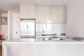 A modern kitchen with white cabinetry, a stainless steel refrigerator, a gas stove, and a sink. - Starry Nights on Lonsdale Steps to Melbourne Icons (Melbourne)
