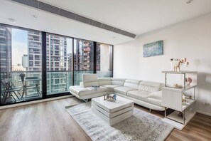 A modern living room with a white sectional sofa, a coffee table, and a glass-top side table with decorative items. - Starry Nights on Lonsdale Steps to Melbourne Icons (Melbourne)