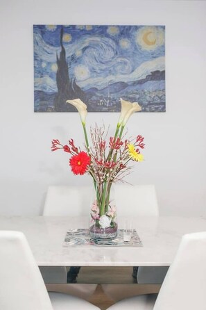 Een eettafel met een bloevas en een schilderij aan de muur.