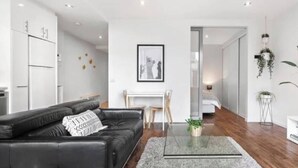 A modern living room with a black leather sofa, a glass coffee table, and a grey rug. - Minimal at Altitude Poolside Stay by CBD Landmarks (Melbourne)