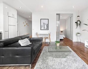 A modern living room with a black leather sofa, a glass coffee table, and a grey rug. - Minimal at Altitude Poolside Stay by CBD Landmarks (Melbourne)