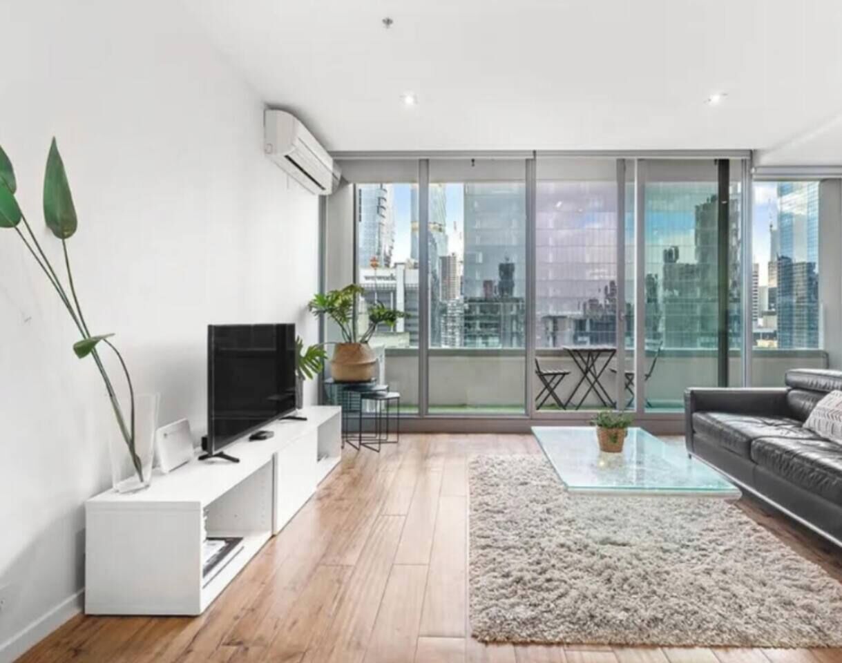 A modern living room with a flat-screen TV, a glass coffee table, and a sofa.