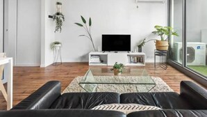 A modern living room with a glass coffee table, leather sofa, and a flat-screen TV. - Minimal at Altitude Poolside Stay by CBD Landmarks (Melbourne)