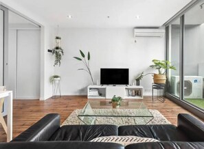 A modern living room with a glass coffee table, leather sofa, and a flat-screen TV. - Minimal at Altitude Poolside Stay by CBD Landmarks (Melbourne)