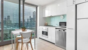 A modern kitchen with white cabinets, stainless steel appliances, and a dining area with a table and chairs. - Minimal at Altitude Poolside Stay by CBD Landmarks (Melbourne)