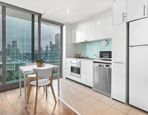 A modern kitchen with white cabinets, stainless steel appliances, and a dining area with a table and chairs. - Minimal at Altitude Poolside Stay by CBD Landmarks (Melbourne)