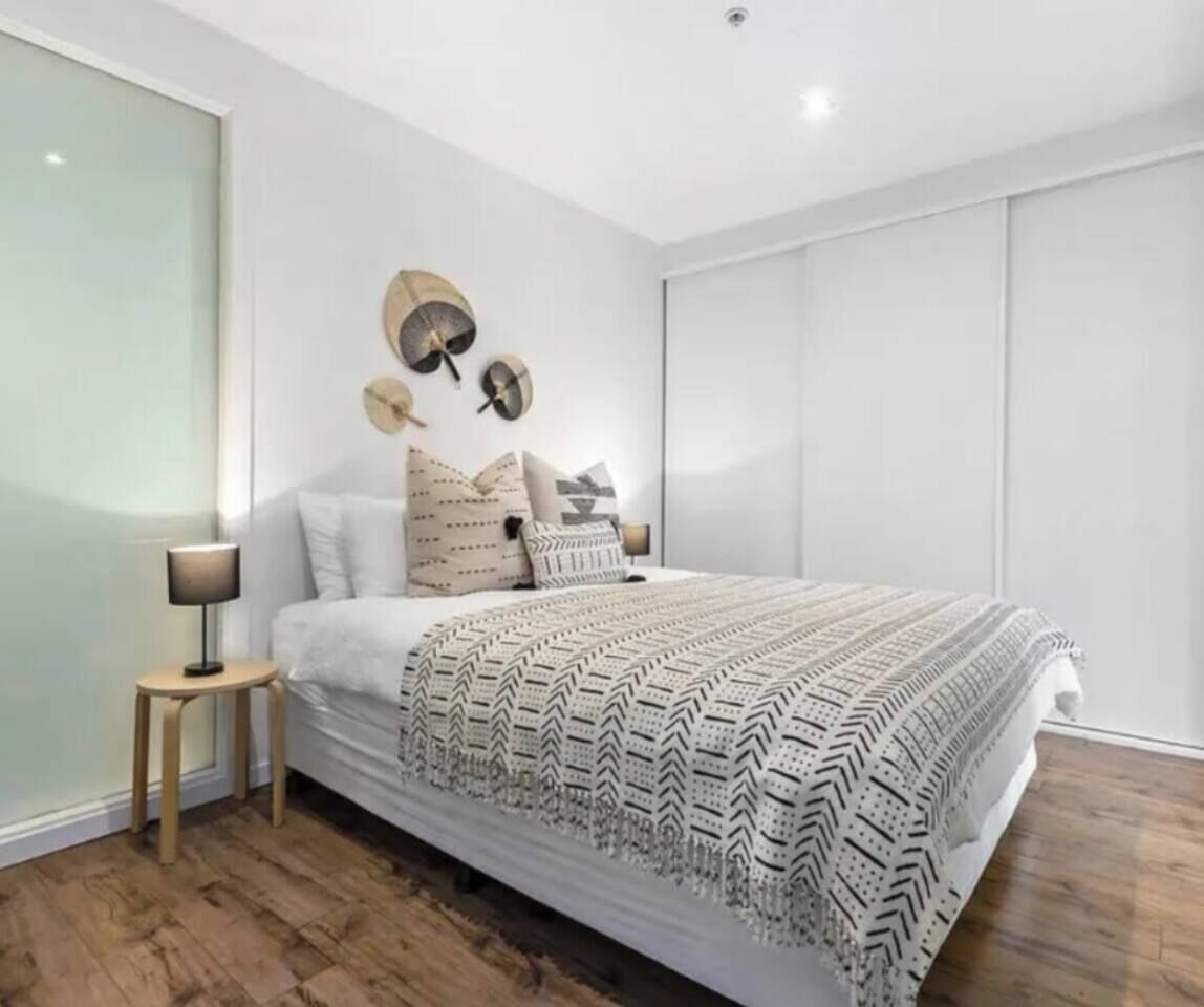 Un dormitorio con una cama grande, una mesita de noche, una lámpara y un aplique de pared.