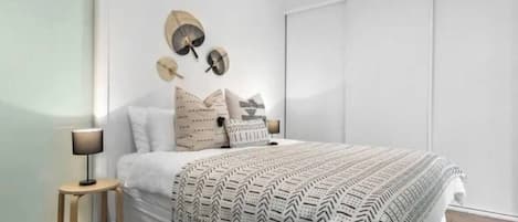 Un dormitorio con una cama grande, una mesita de noche, una lámpara y un aplique de pared.