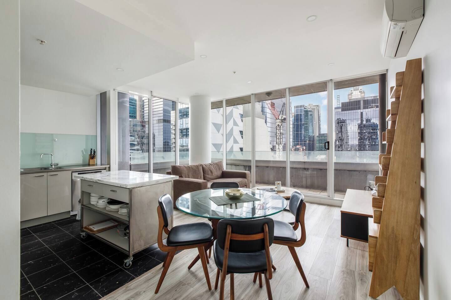 A modern apartment with a dining area, kitchen, and large windows offering city views.