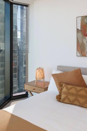 A bedroom with a bed, a window, a chair, and a painting on the wall. - Southbank Sojourn Resort Comfort and Skyline Views (Southbank)